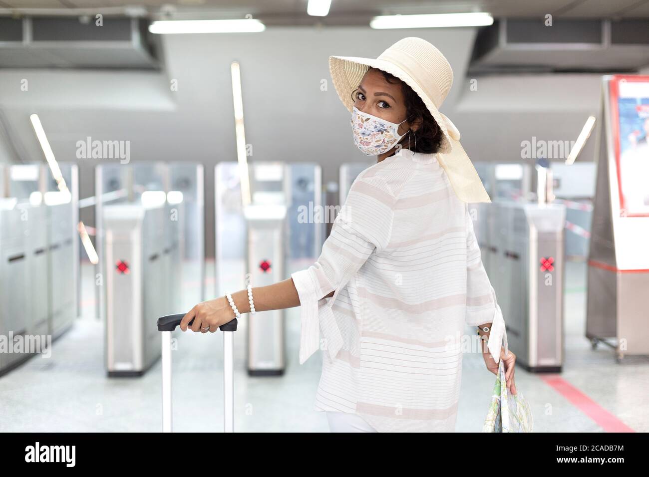 Eine lateinische Frau mit Koffer, einer Touristenkarte und einer Gesichtsmaske, die bereit ist, während eines Coronavirus-Ausbruchs auf eine Reise zu gehen. Sicheres Reisekonzept. Stockfoto