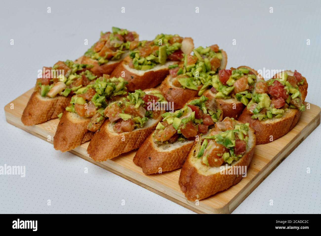 Schließen Sie viele Tapas auf Holzbrett. Spanisches Essen. Lachsfisch und Avocado-Salat auf geröstetem Brot. Verwischen Sie weißen Hintergrund Stockfoto