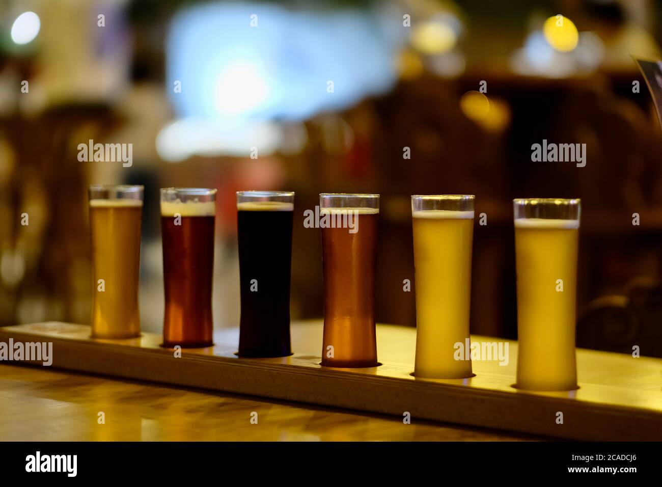Auf dem glänzenden Holztisch in der Bar können Sie verschiedene Biersorten in Pint-Gläsern aus der Nähe betrachten. Gekleidete Gläser Bier in verschiedenen Farben. Hintergrund verwischen Stockfoto