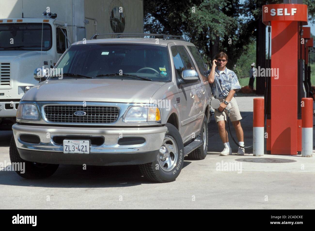 Austin Texas USA: Anglo-Mann spricht am Handy, während er an der Tankstelle ein benzinkendes Sportfahrzeug auffüllt. ©Bob Daemmrich Stockfoto