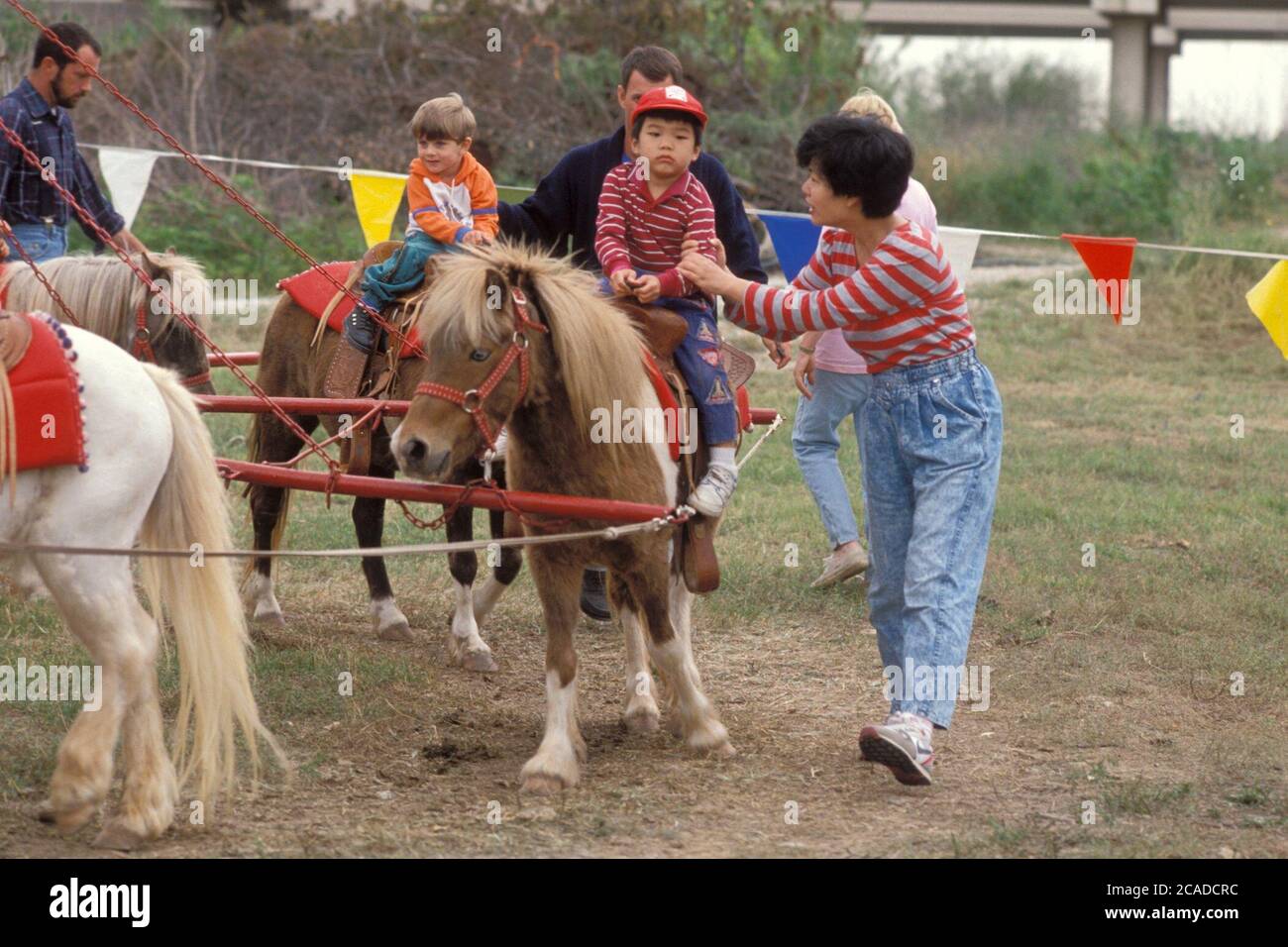 Der asiatisch-amerikanische Junge sitzt auf einem Pony, während seine Mutter neben ihm läuft, um ihn beim Kinderfest im Austin Nature Center vor dem Abfallen zu bewahren. ©Bob Daemmrich Stockfoto