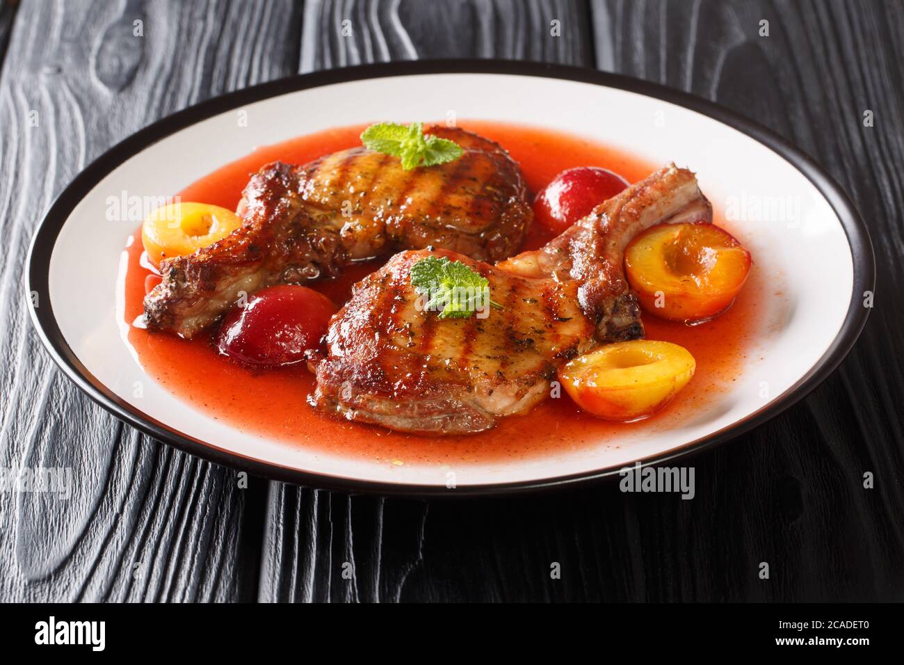 Portion gegrilltes Schweinekotelett mit Pflaumen und Obstsoße in Nahaufnahme in einem Teller auf dem Tisch. Horizontal Stockfoto