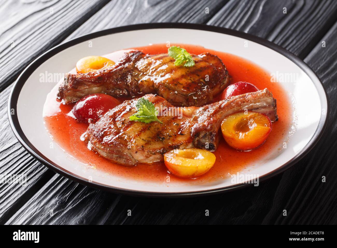 Gourmet-Rezept für gegrilltes Schweinekotelett mit Pflaumen und Obstsauce close-up in einem Teller auf dem Tisch. Horizontal Stockfoto