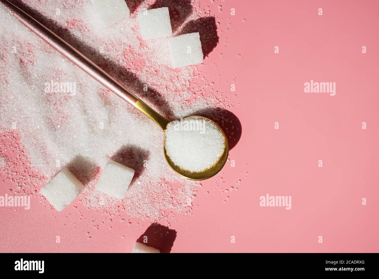 Weißer Zucker im Löffel und Zuckerwürfel auf rosa Stockfoto