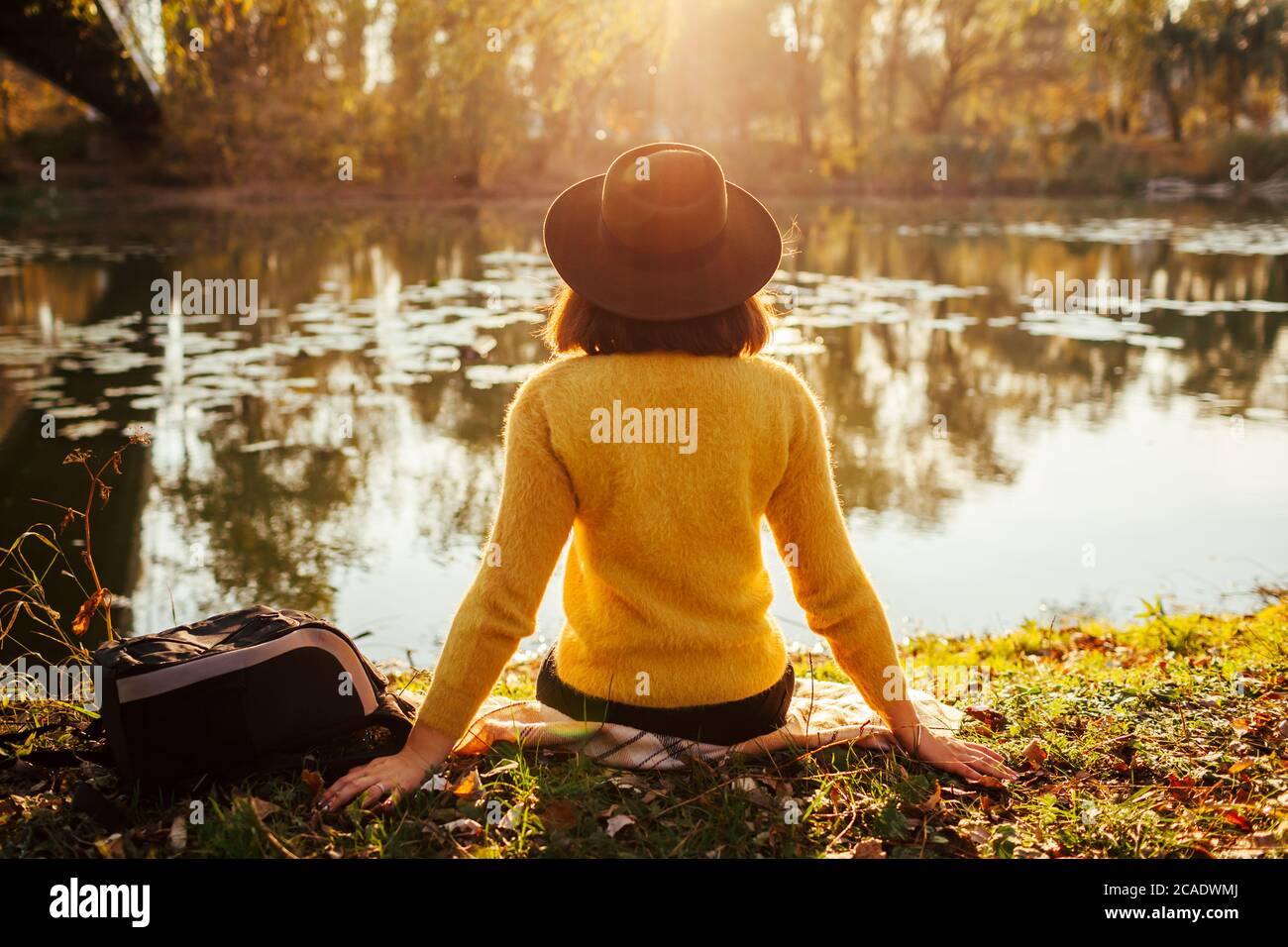 Frau, die sich am Herbstfluss bei Sonnenuntergang entspannt. Mädchen sitzt auf Bank von Brücke genießen Landschaft Stockfoto