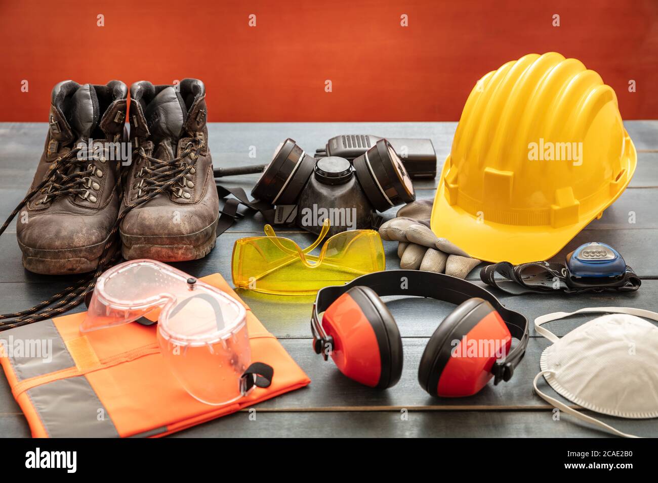 Arbeitsschutzausrüstung. Industrielle Schutzausrüstung auf Holztisch, roter Hintergrund. Baustellen-Gesundheits- und Sicherheitskonzept Stockfoto