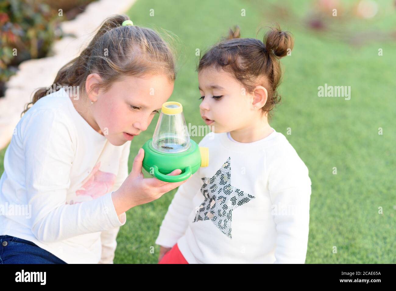 Zwei nette neugierige Kinder Kinder im Sommerurlaub Spaziergang im Innenhof, Blick auf Caterpillar durch Hand Vergrößerungsglas im Freien. Kleines Mädchen hält ein Insekt. Stockfoto