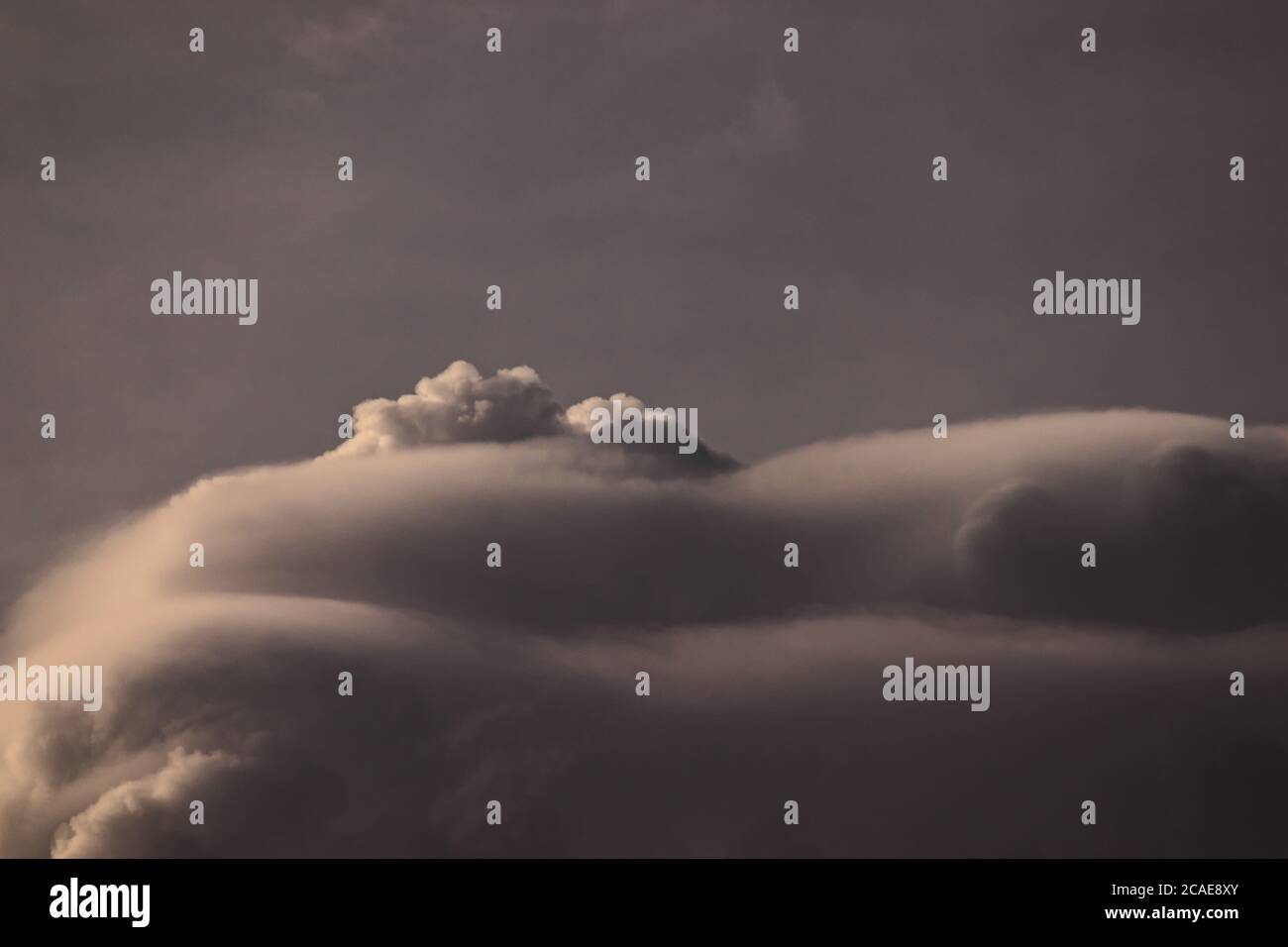 Große graue Cumulus Wolken fast vollständig von Pileus bedeckt, schwimmend unter einem bewölkten Himmel. Stockfoto