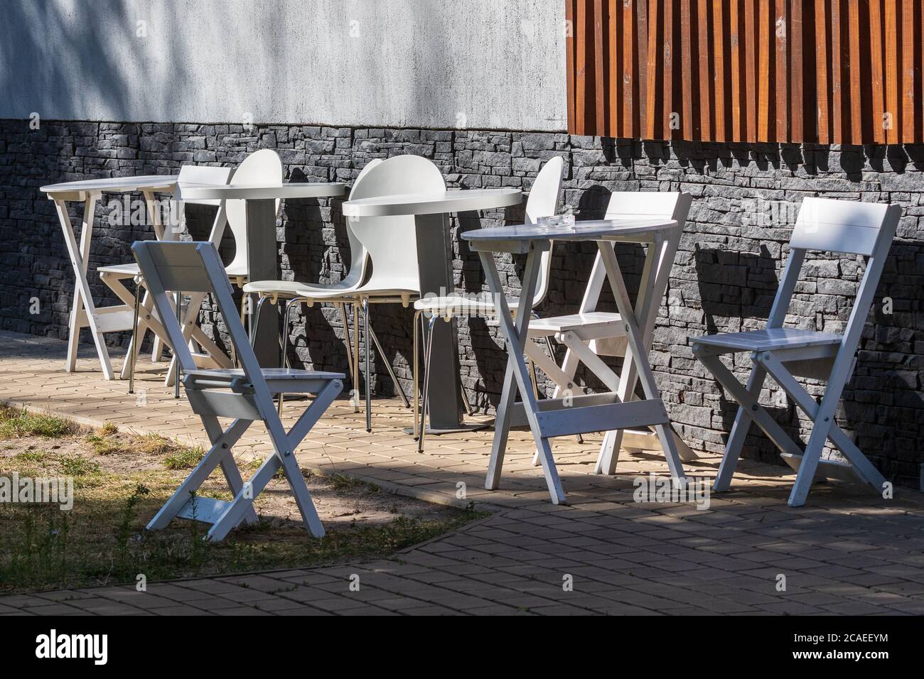 Tische und Stühle aus weißem Holz stehen an einem sonnigen Sommertag ohne Besucher an einer grauen Steinmauer. Der Terrassenbereich des Coffeeshops. Ein gemütliches Café. Ein Ort t Stockfoto