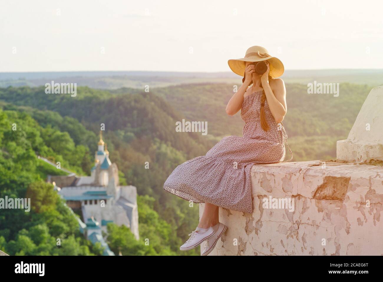 Mädchen sitzt auf einem Hügel und macht Bilder gegen einen Wald und Tempel Stockfoto