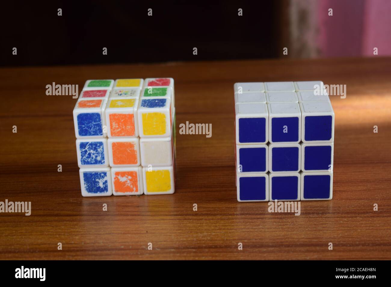 Nahaufnahme eines ungelösten und gelösten Rubik's Cubes auf einem Holztisch mit verschwommenem Hintergrund Stockfoto