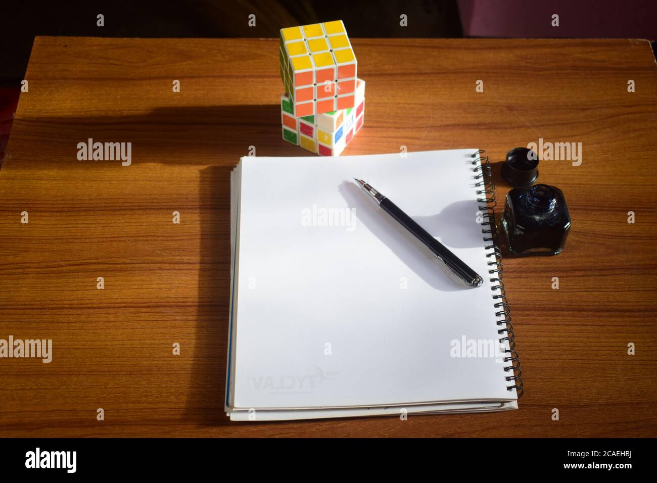 High-Angle-Ansicht der gelösten und ungelösten Rubik's Würfel auf Ein Tisch mit einem Notizblock und einem Tintenstift auf IT Stockfoto