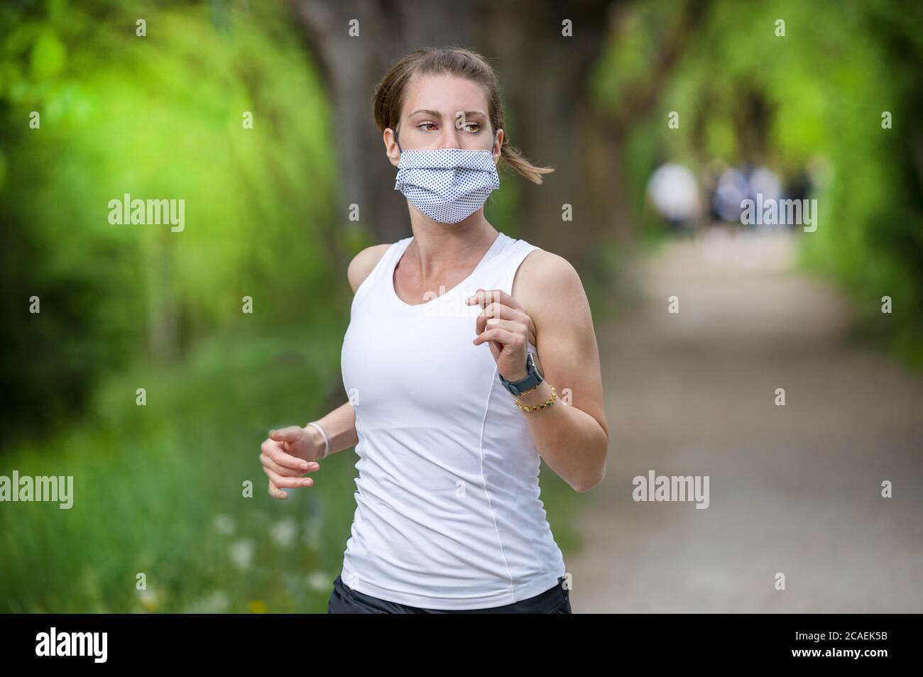 Bleiben Sie während des Coronavirus fit. Eine sportliche Frau joggt draußen, sie hat eine Schutzmaske im Gesicht. Laufen in den Tagen des Covid-19. Stockfoto