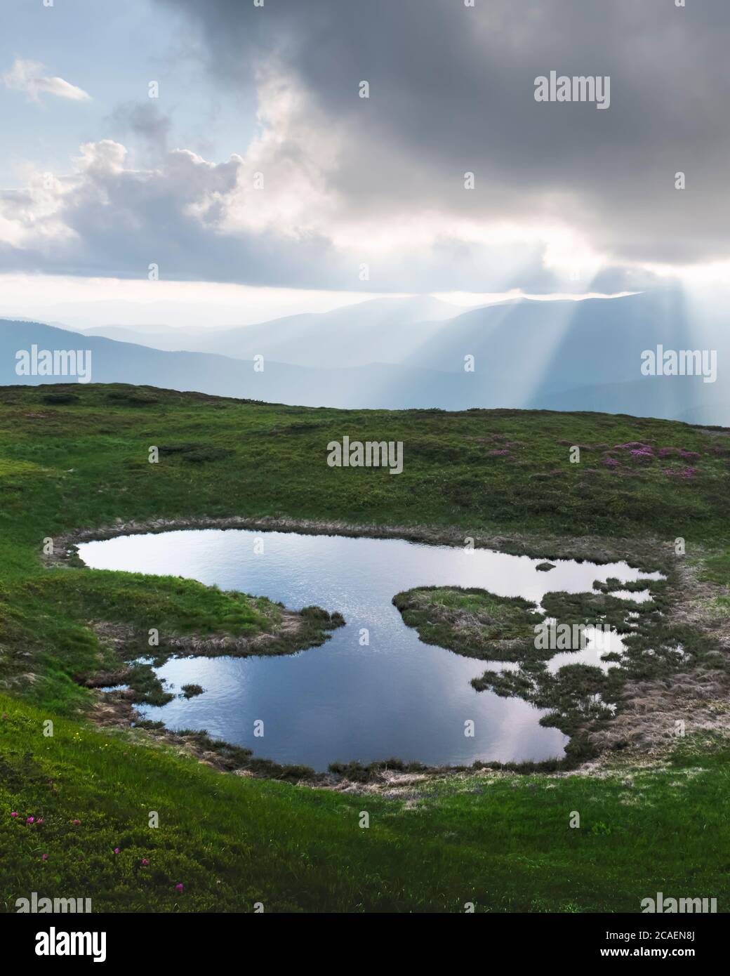 Bergsee bei Sonnenaufgang. Malerische Sommerlandschaft mit grünen Hügeln und Sonnenstrahlen am Morgenhimmel. Karpaten Stockfoto