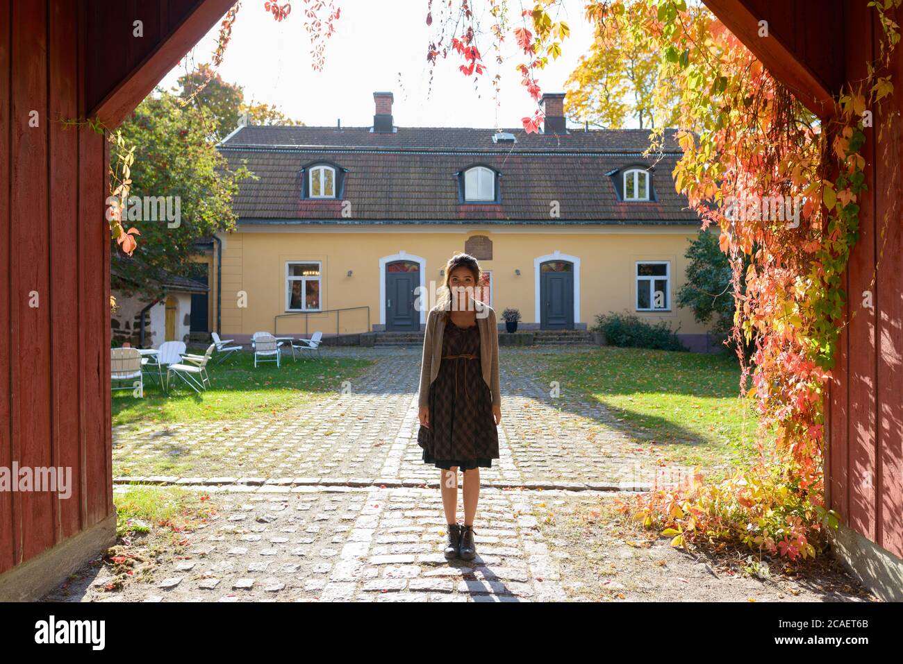 Junge glückliche asiatische Frau lächelnd und stehend im hölzernen Eingang des eleganten Vorstadthauses Stockfoto