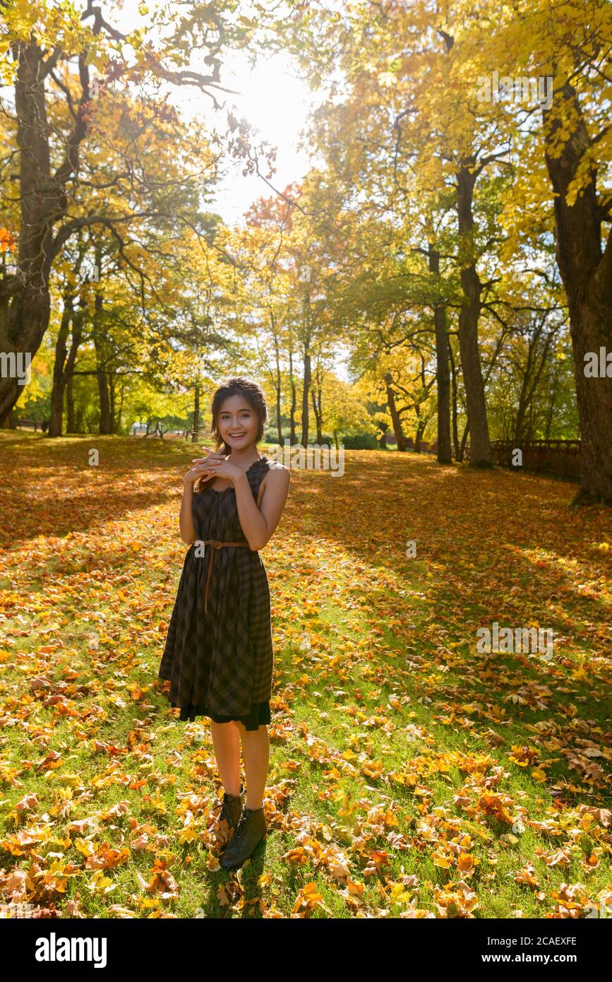 Junge glückliche asiatische Frau lächelt gegen Blick auf den Wald im Herbst Stockfoto