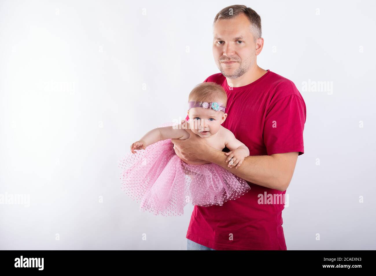 Junger Mann, der seine Tochter in den Armen hält, schönes und gesundes Baby in rosa Rock und Schmuck auf dem Kopf Stockfoto