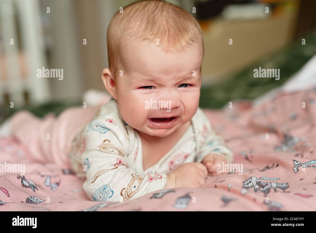 Drei Monate altes Mädchen weinend, liegt auf dem Bauch und ist sehr aufgeregt, traurige Emotionen im Kind Stockfoto