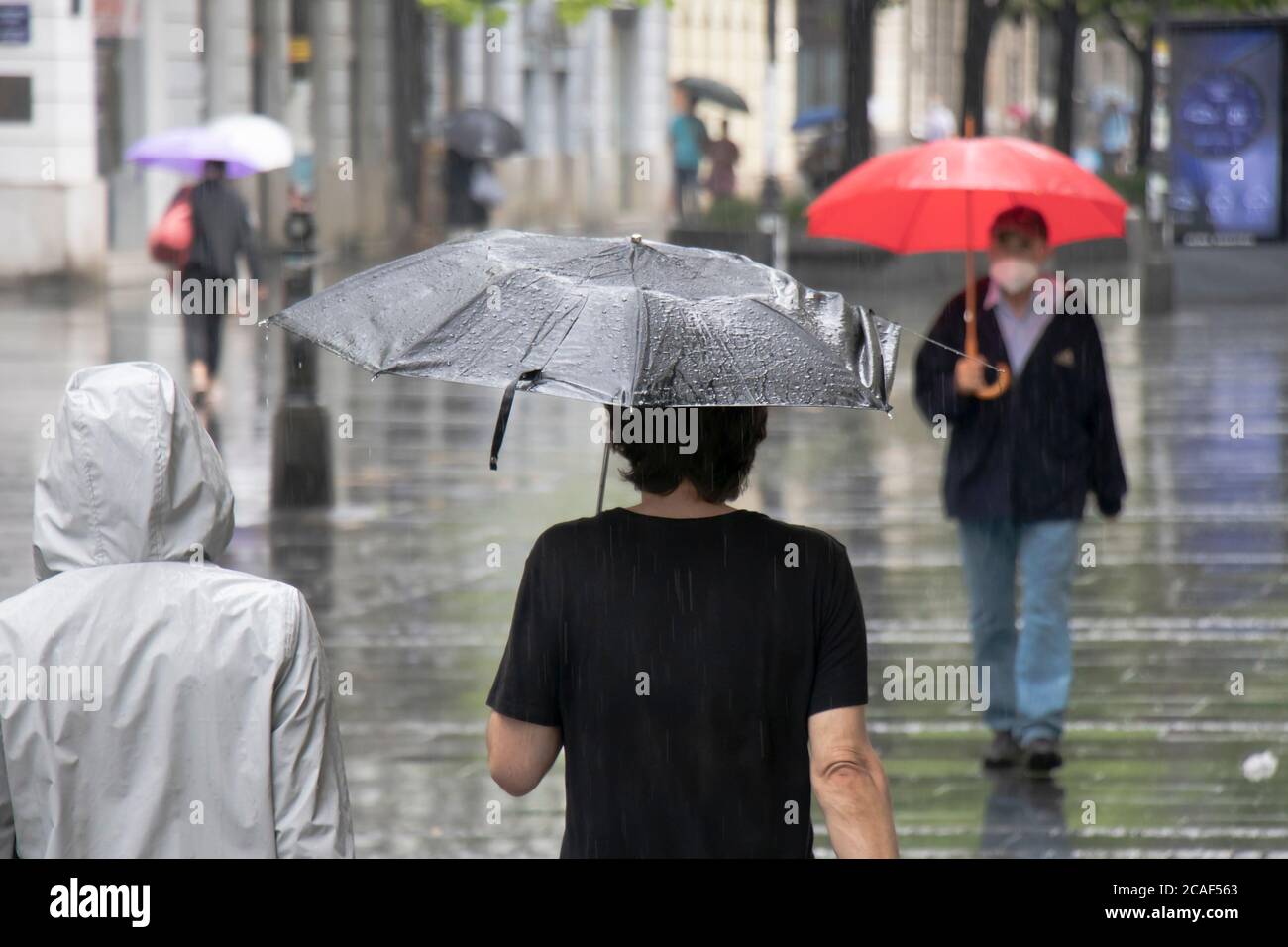 Menschen unter Sonnenschirmen gehen an einem regnerischen Sommertag in der Stadt Belgrad, Serbien, durch die Fußgängerzone Stockfoto