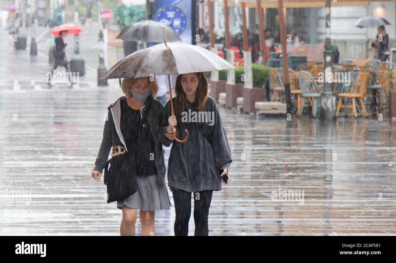 Belgrad, Serbien - 5. August 2020: Menschen unter Sonnenschirmen gehen an einem regnerischen Sommertag in der Stadt auf der Fußgängerzone Stockfoto