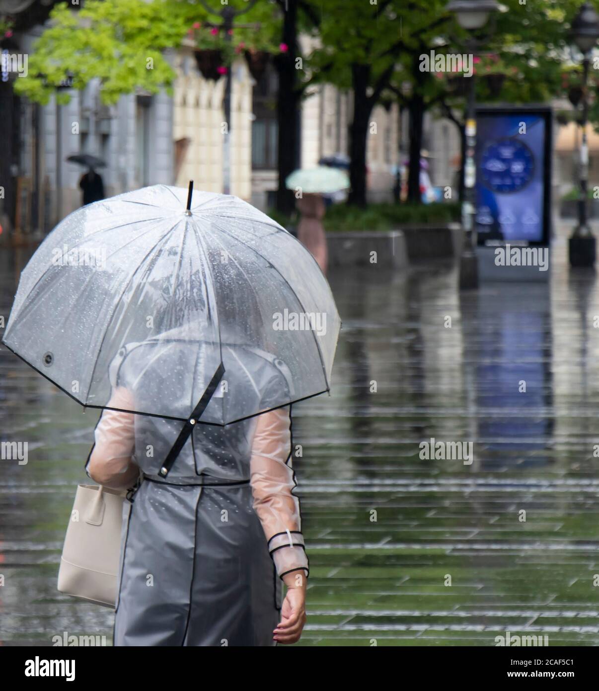 Frau in transparentem Regenmantel, die an einem regnerischen Sommertag in Belgrad, Serbien, unter dem Regenschirm läuft Stockfoto