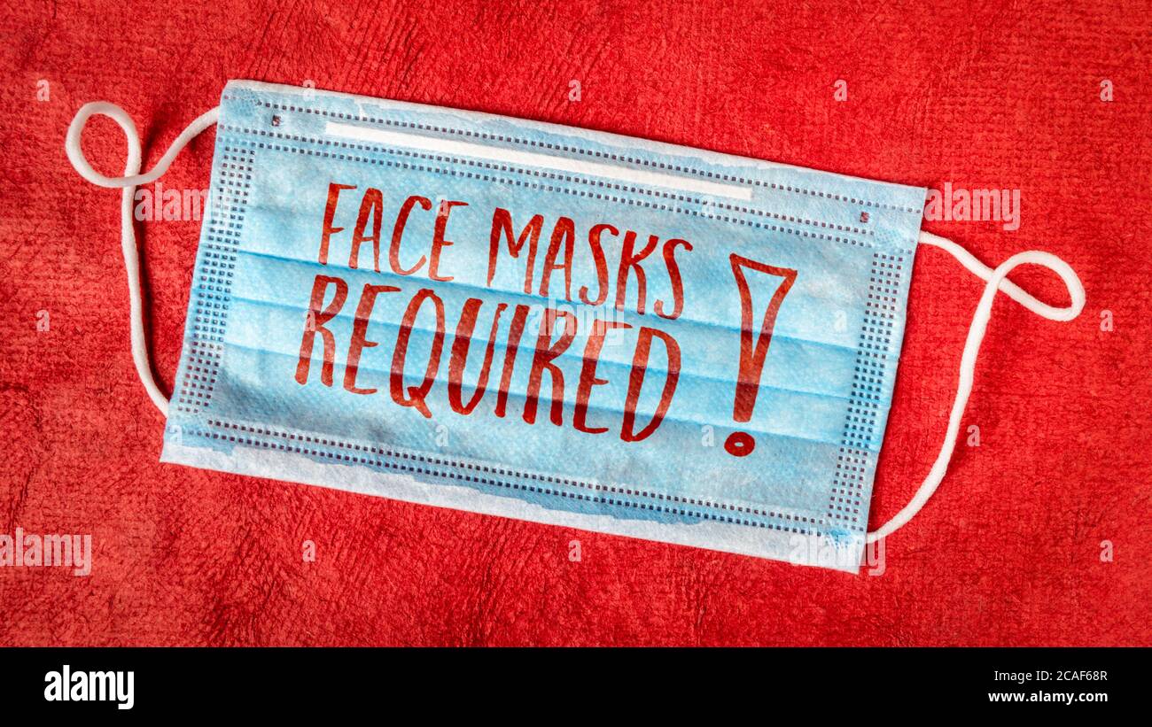 Gesichtsmasken erforderlich - Text auf einer Einwegmaske gegen rotes strukturiertes Papier, Geschäftszeichen während der Coronavirus covid-19 Pandemie und soziale Distanci Stockfoto