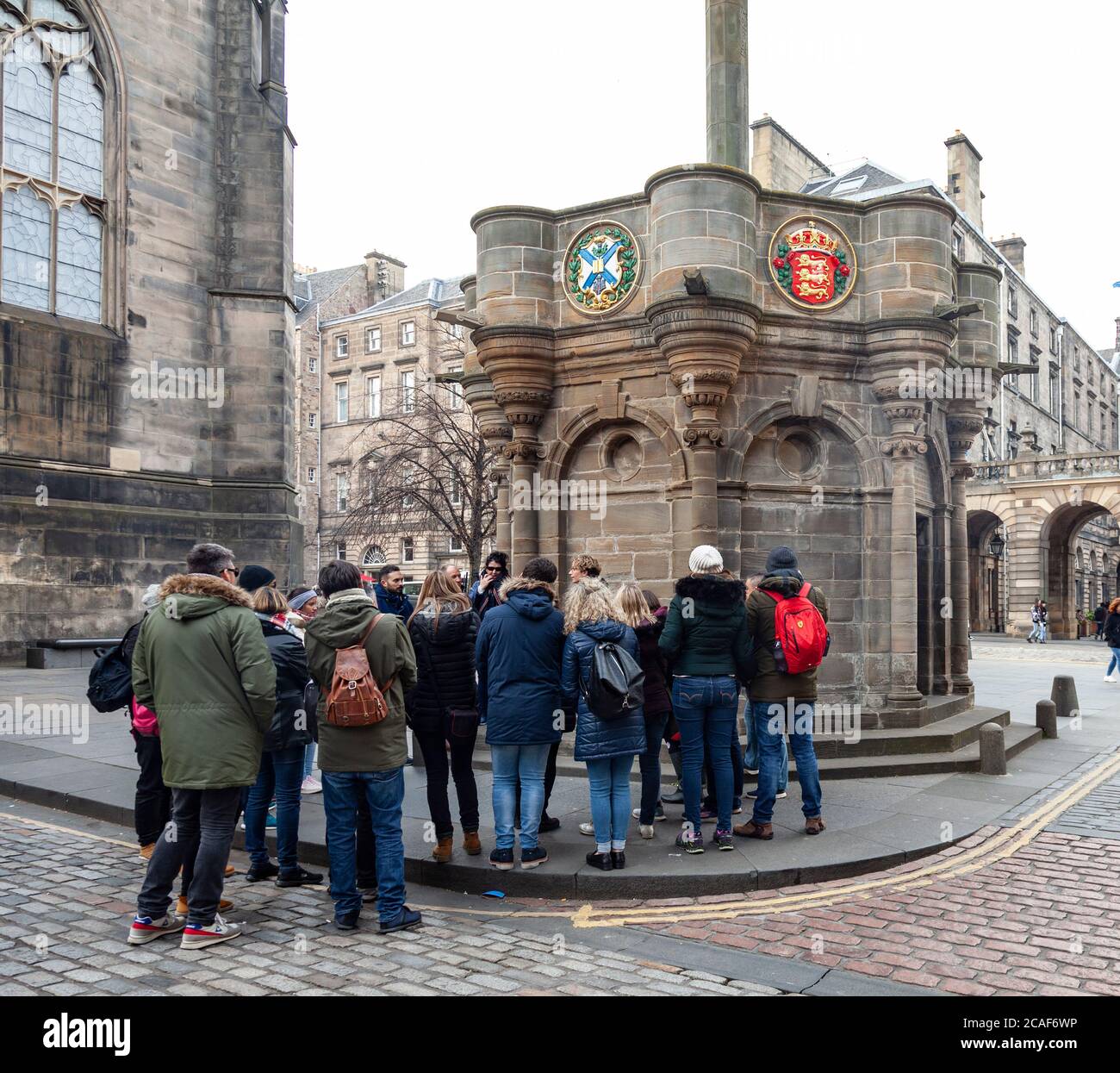 Eine Reisegruppe, die ihrem Fremdenführer vor dem Mercat Cross neben der St Giles Cathedral in der Royal Mile / High Street, Edinburgh, Schottland, Großbritannien zuhört Stockfoto
