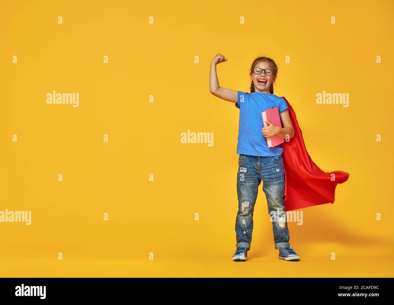 Kleines Kind spielt Superheld. Kind auf dem Hintergrund der hellen Farbe Wand. Bildung und Erfolgskonzept. Gelb, rot und blau. Stockfoto