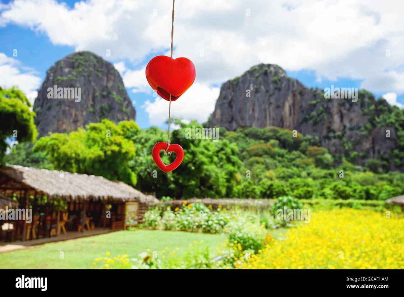 Dekorieren Zeug als rote Herz Mobile ist Schaukel in der Luft mit gelben Kosmos und großen Berg Hintergrund. Stockfoto