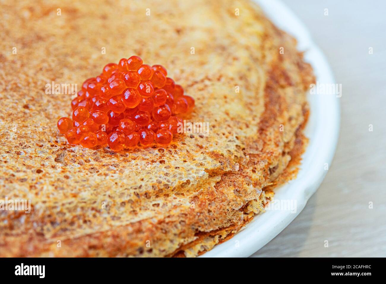 Traditionelle russische Pfannkuchen mit rotem Kaviar auf weißem Teller Ein Holztisch Stockfoto
