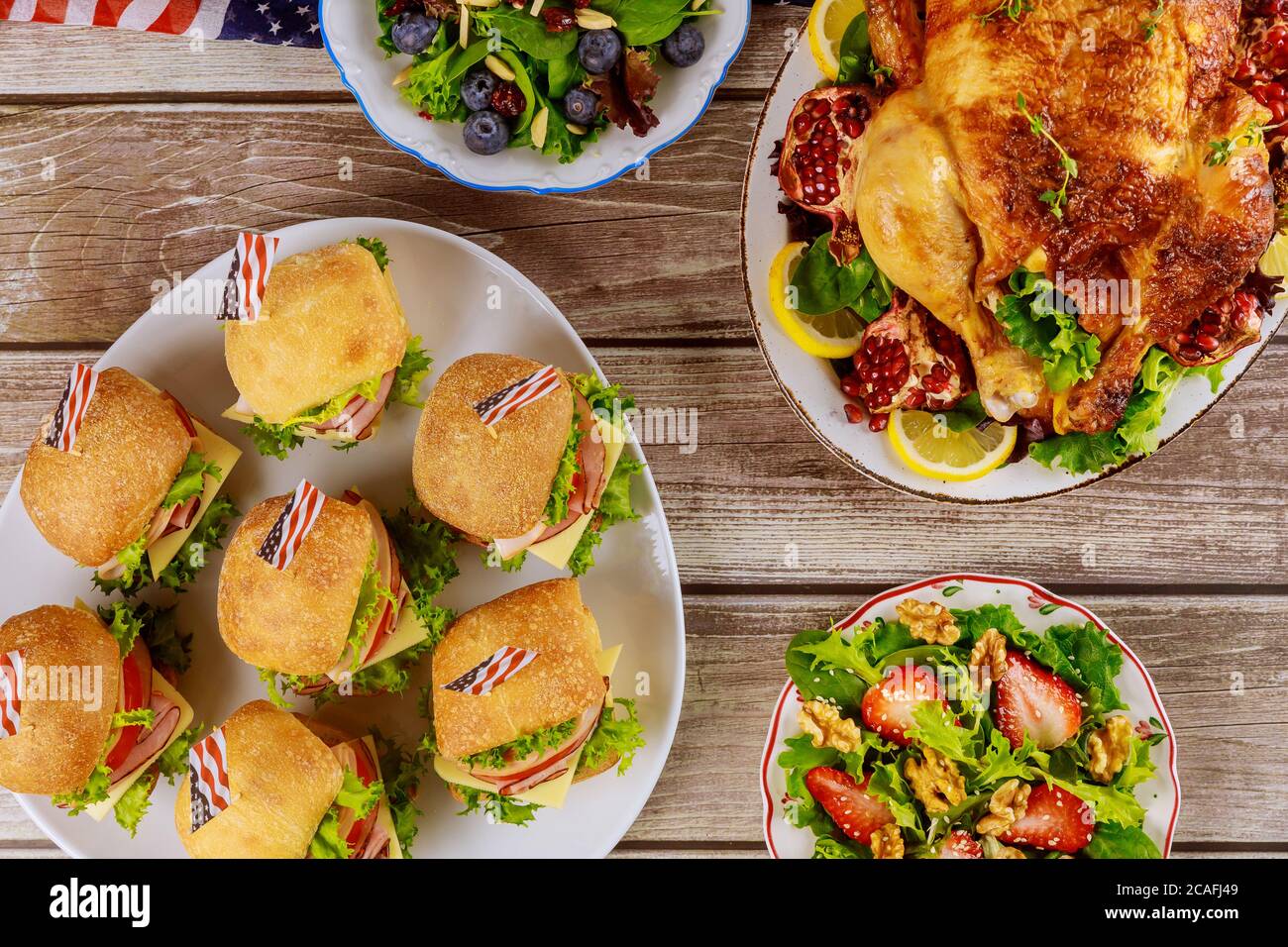 Huhn, Sandwiches und Salat auf Holztisch mit amerikanischen Flaggen. Stockfoto