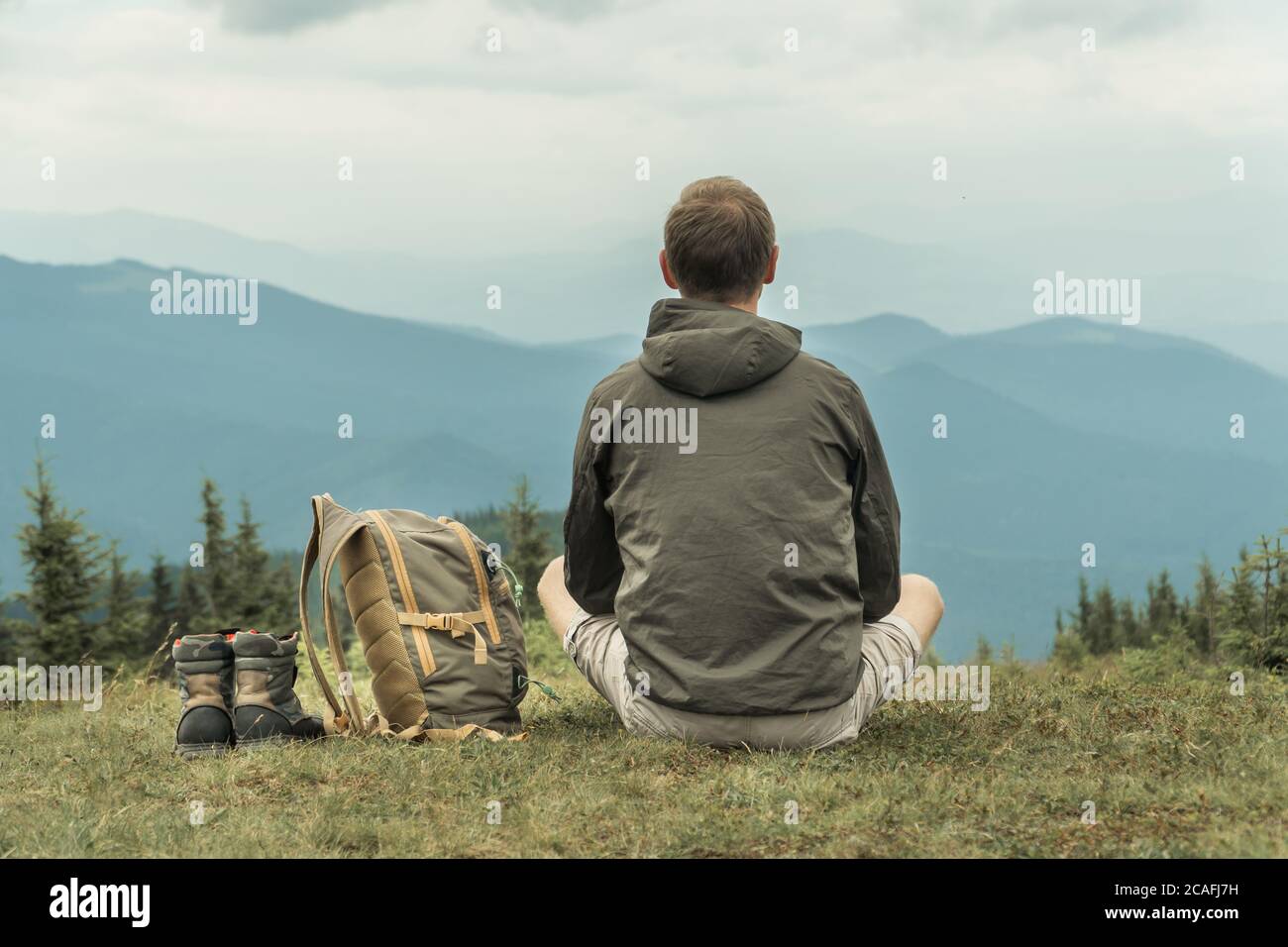 Wandertourist sitzt auf einem Berg Hügel Blick auf die Berge mit einem Rucksack und Stiefel neben ihm stehen Stockfoto
