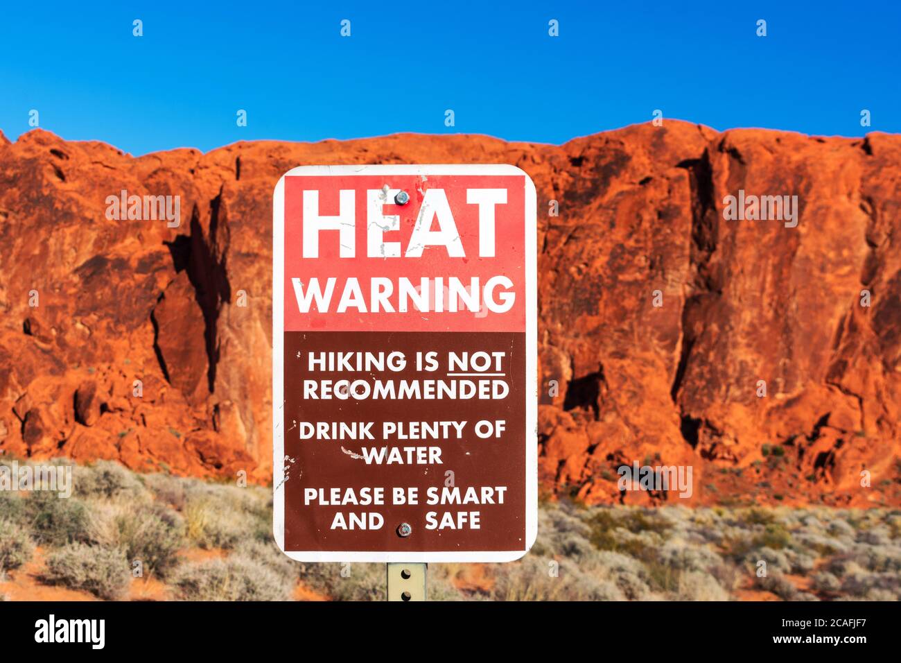 Hitzewarnschild informiert Touristen über die Gefahren der Hitzeerschöpfung beim Wandern im Wüstenklima. Verschwommene malerische rote Sandsteinformationen und de Stockfoto