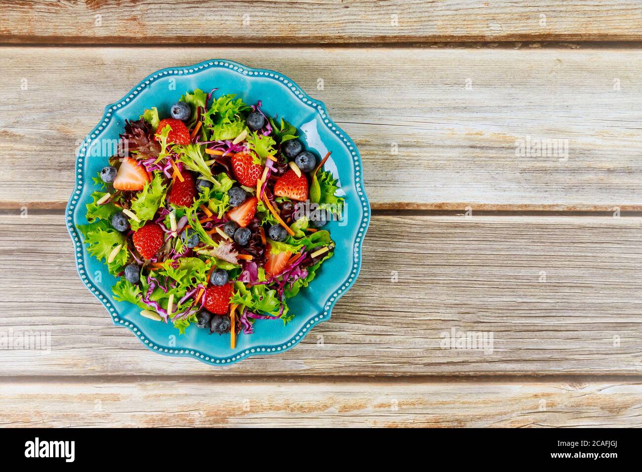 Gemischter Salat mit Beeren, grünen Blättern, Karotte, Heidelbeere und Mandel auf blauem Teller. Stockfoto