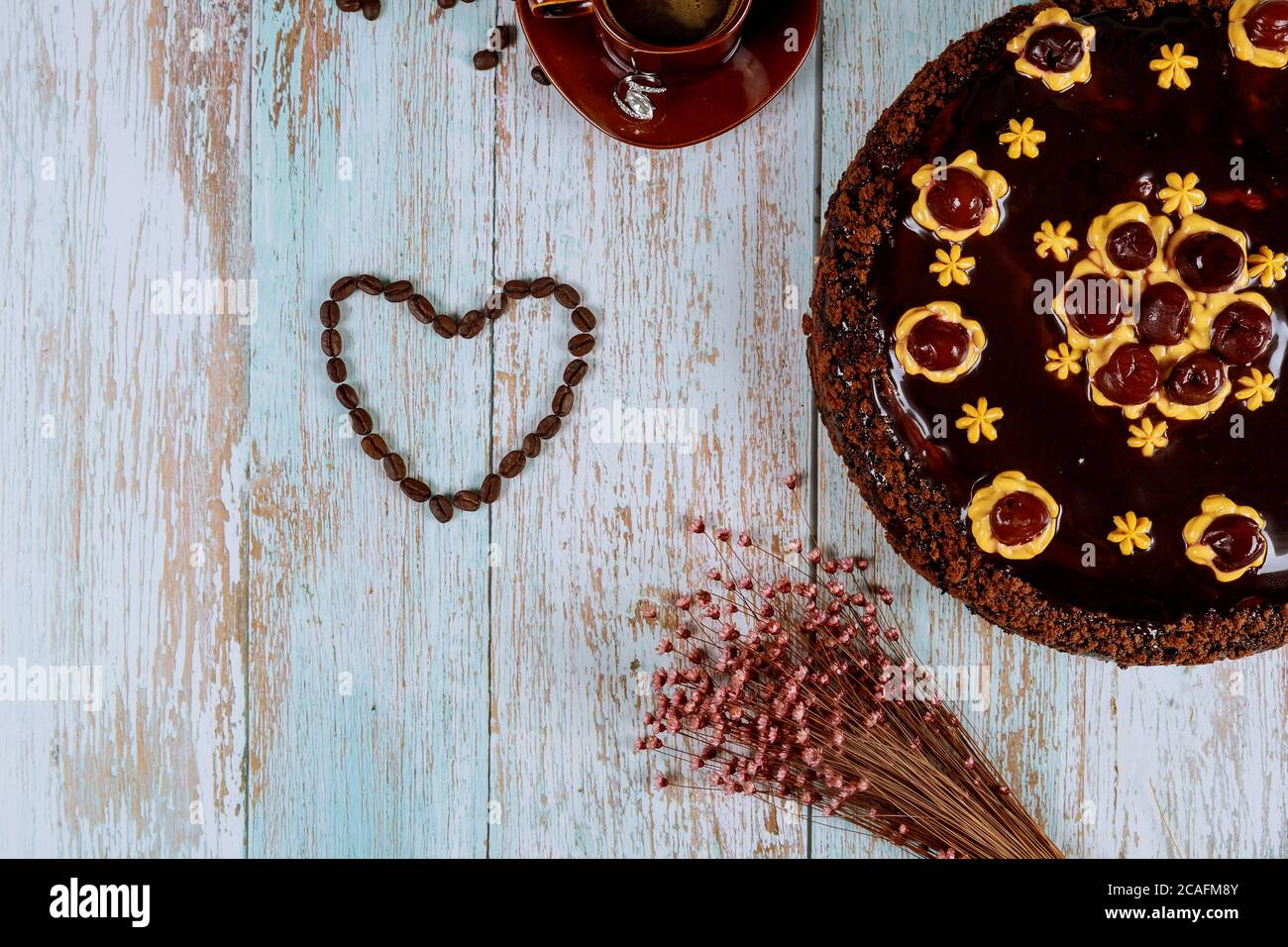 Herzform aus Kaffeebohnen mit Schokoladenkirschkuchen mit Blumen und Tasse Kaffee. Stockfoto