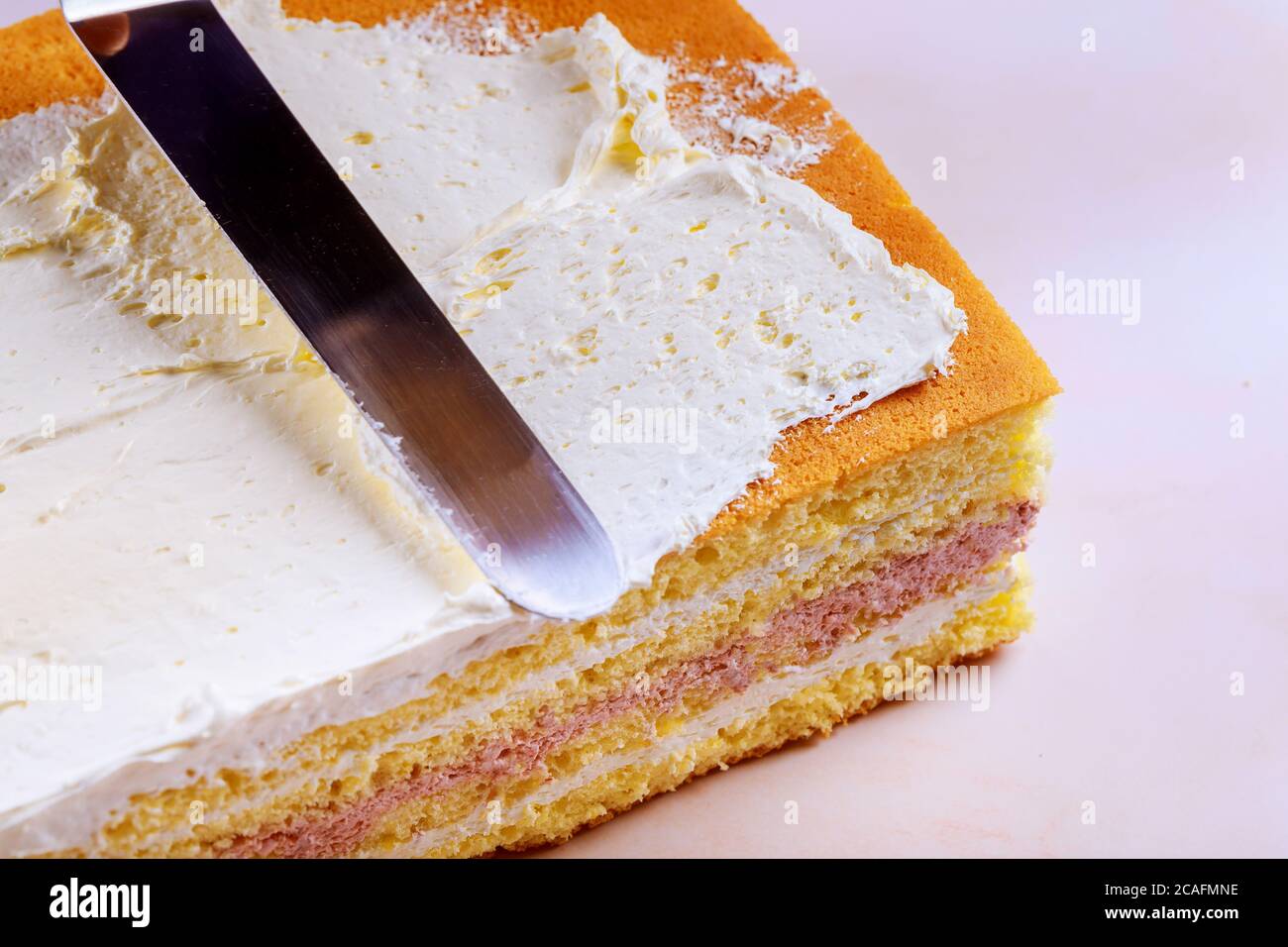 Kuchen mit Biskuit oder Biskuit mit weißer Sahne mit einem Kochspatel zubereiten. Stockfoto