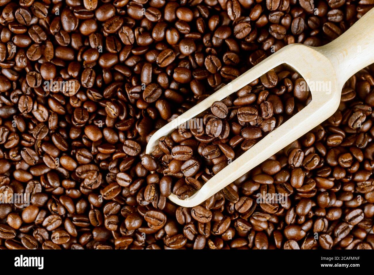 Schwarze Kaffeebohnen Hintergrund mit Holzlöffel. Stockfoto