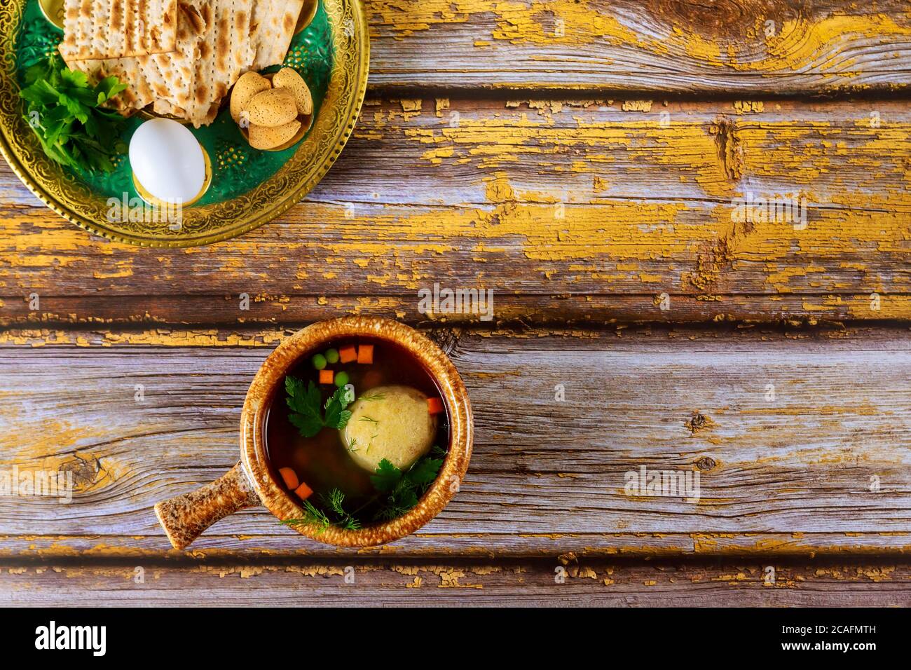 Traditionelle jüdische Matzoballsuppe und Sederteller auf Holztisch für Passah. Stockfoto