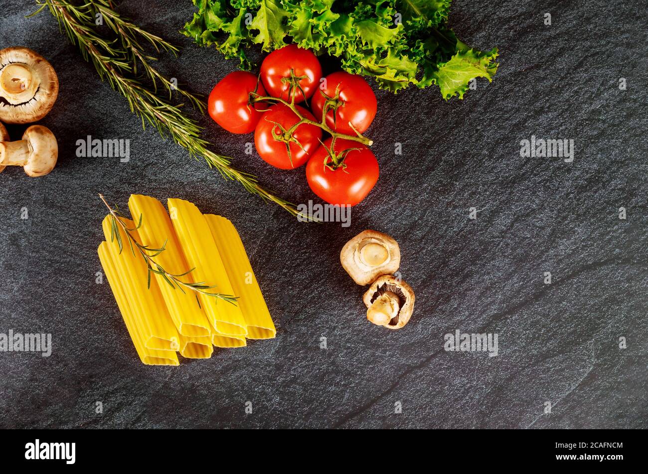 Bio Pasta Manicotti mit Pilzen und Tomaten auf schwarzem Hintergrund. Stockfoto