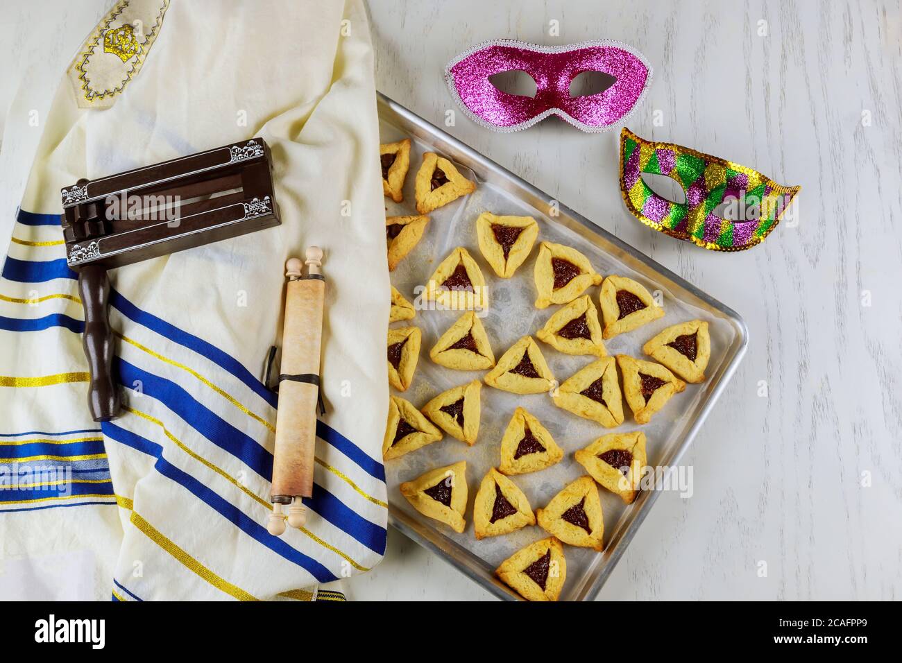 Jüdische Dreieckskekse mit Marmelade für Purim mit Maske, Tallit und Noisemaker mit tora. Stockfoto