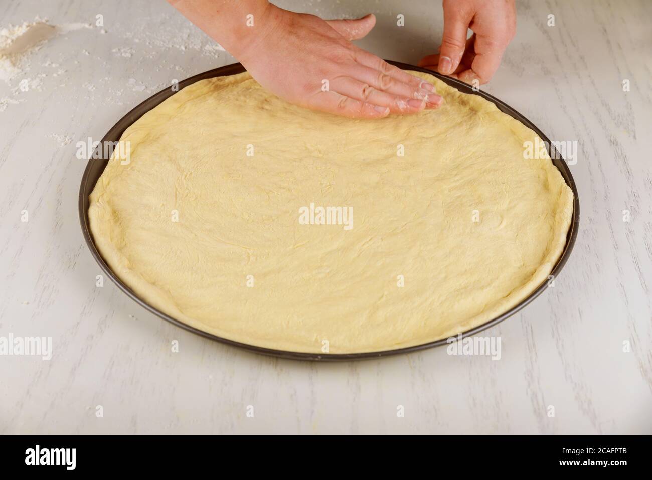 Frau drückt auf frischen rohen Pizzateig in der Ofenpfanne. Stockfoto