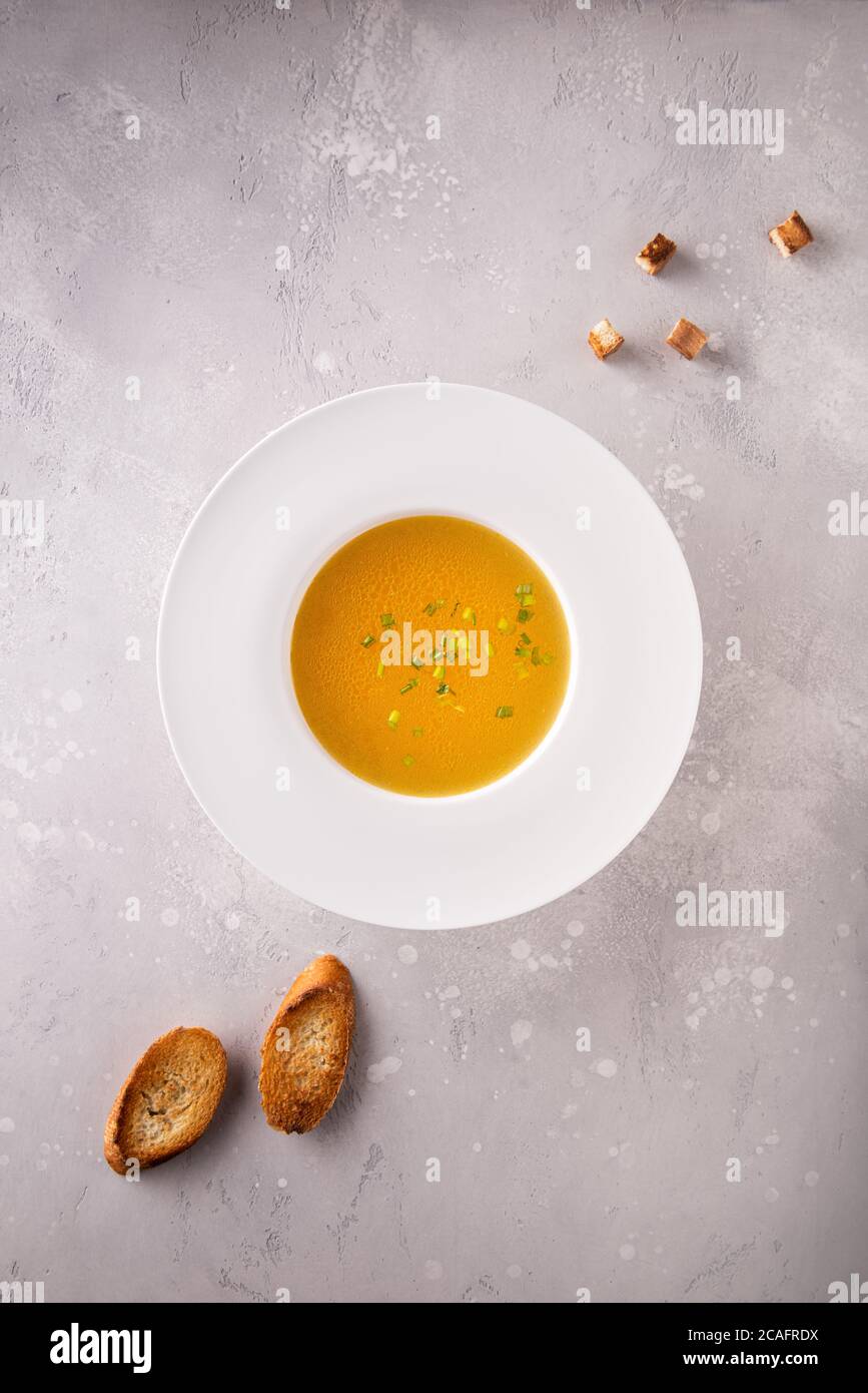 Hühnerbouillon mit gehackten grünen Zwiebeln in weißem Hutteller, einigen Croutons und geröstetem Baguette. Flach legen auf grau strukturierten grauen Stein Hintergrund. Cop Stockfoto