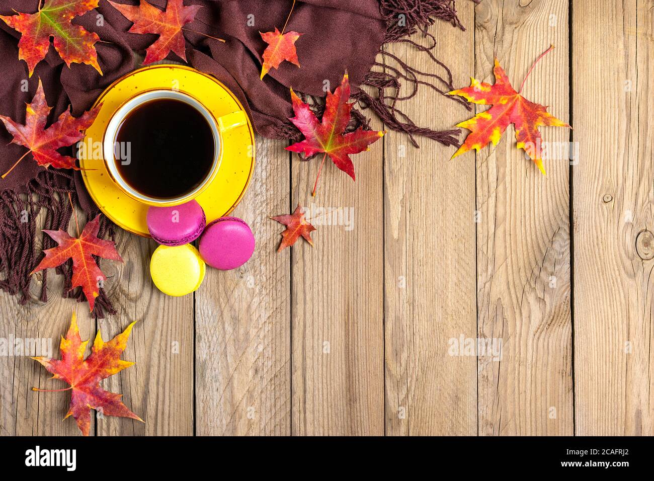 tasse mit heißem schwarzen Kaffee, Schal, Makronen auf Holztisch mit Herbst gefallenen gelben, orangen und roten Blättern Flat Lay Draufsicht Mock Up Hallo september Stockfoto