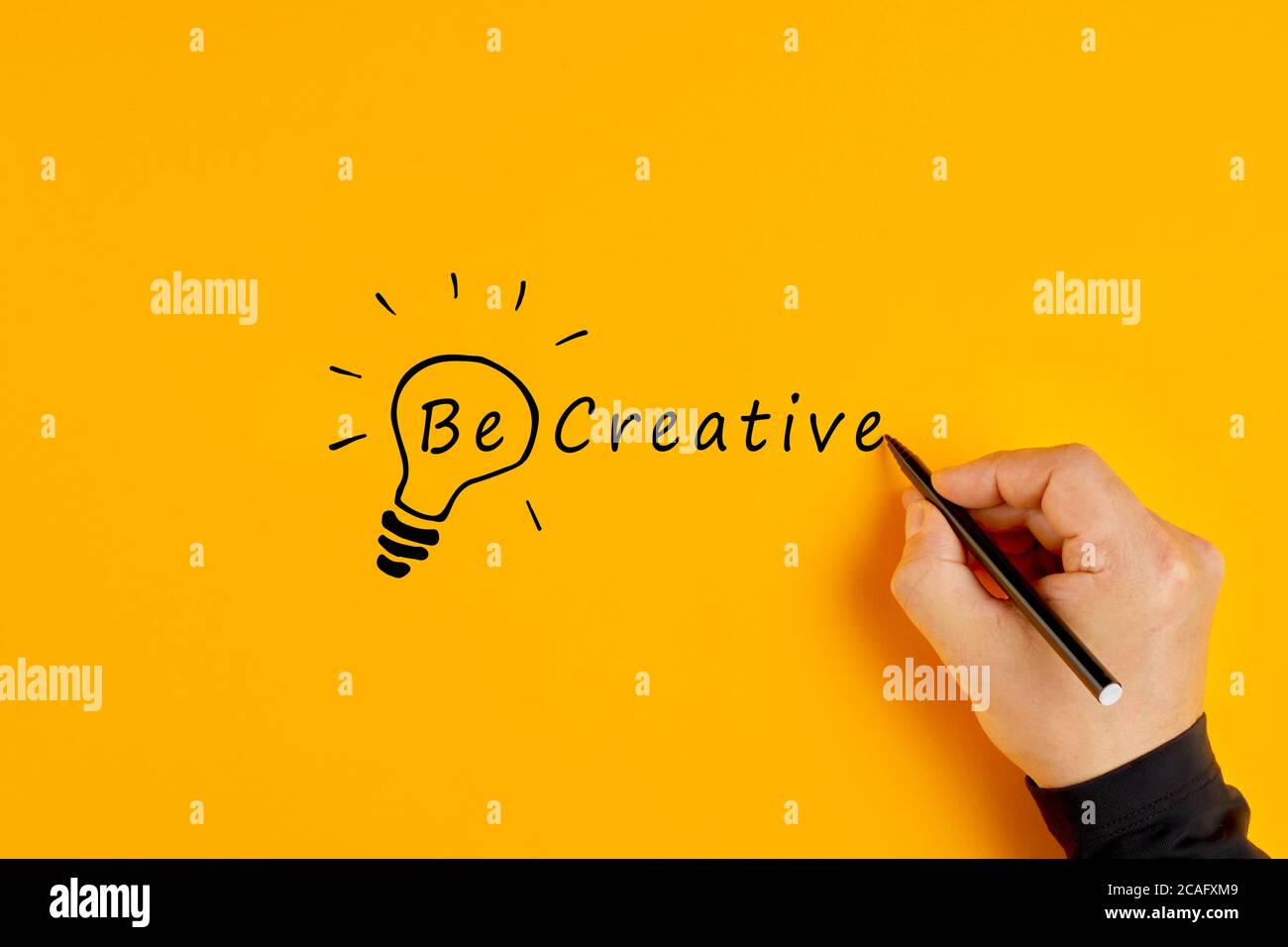 Männliche Hand schreibt die Worte seien Sie kreativ und zeichnet eine Glühbirne auf gelbem Hintergrund. Kreativität und Innovation. Stockfoto
