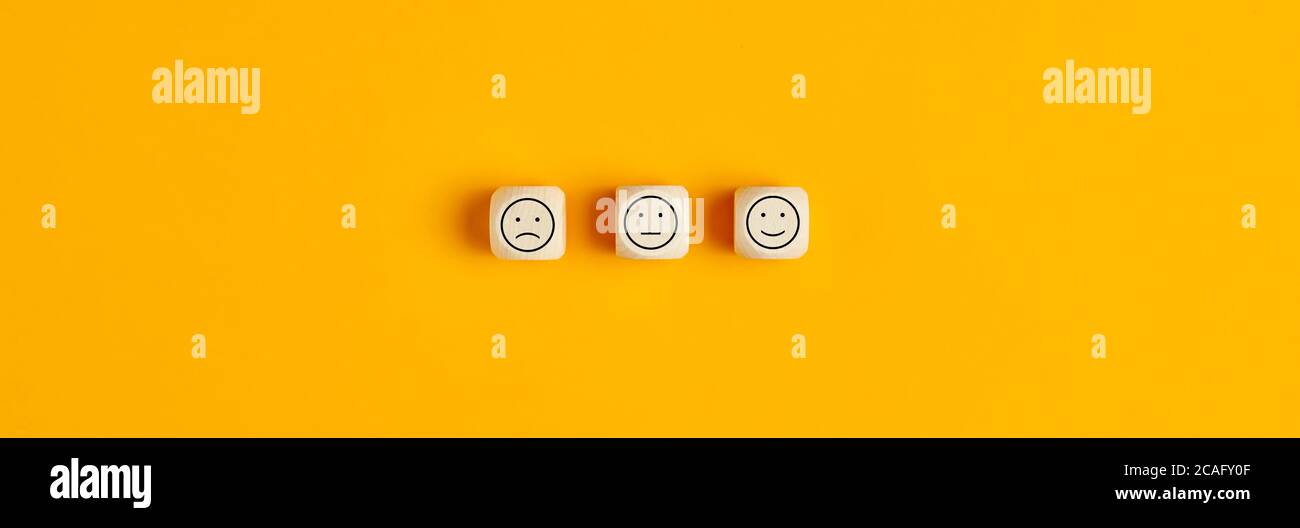 Glücklich traurig und neutral Smiley Gesichter auf Holzblöcken auf gelbem Hintergrund. Kundenzufriedenheit, Bewertung oder Feedback-Konzept. Stockfoto