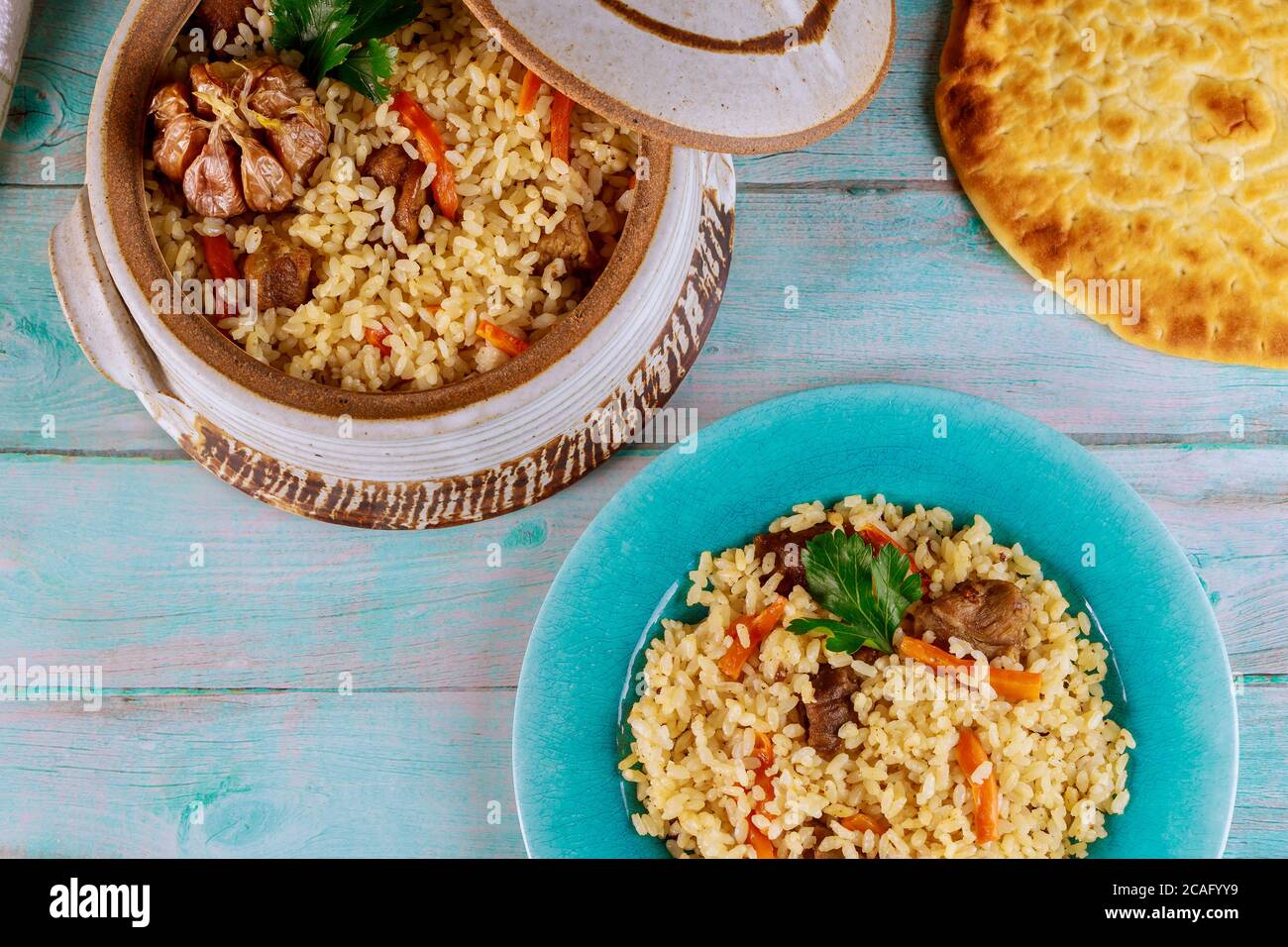 Usbekischer Pilaf mit Reis, Fleisch, Karotten und Knoblauch in Tontopf mit Fladenbrot. Stockfoto