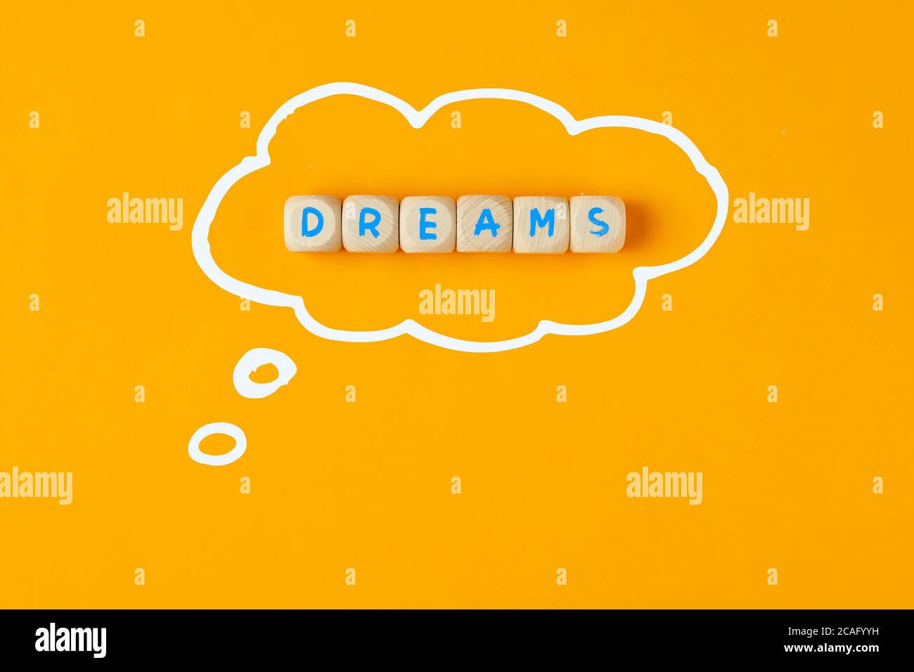Das Wort Träume auf Holzwürfeln geschrieben und mit Gedankenblase auf gelbem Hintergrund eingerahmt. Zukünftige Ansprüche auf Leben, Karriere oder Geschäftskonzept Stockfoto