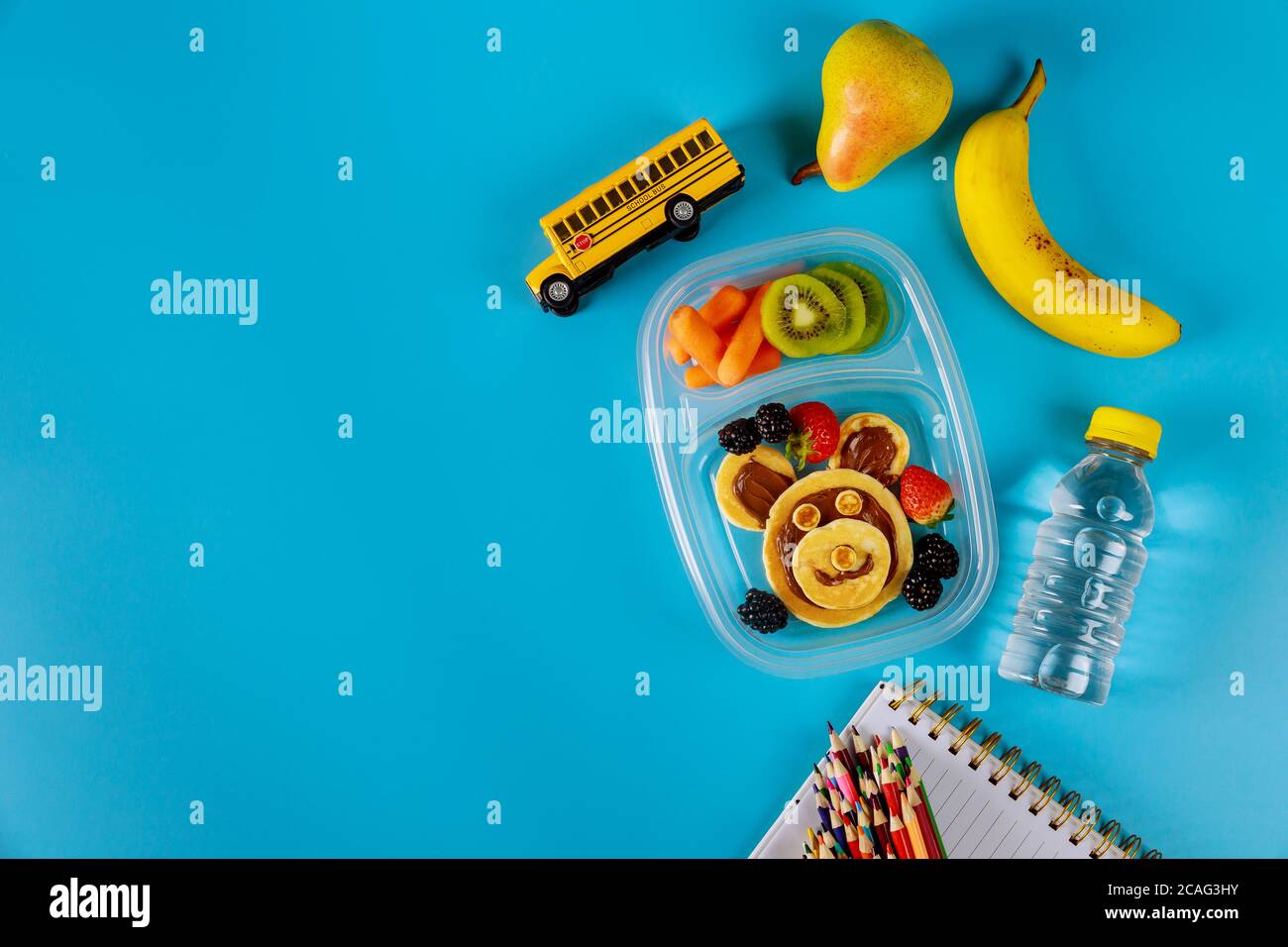Lunchbox mit Pfannkuchen, Karotte, Birne und Banane mit Kinderschrubben. Zurück zur Schule Konzept. Draufsicht, Kopierbereich. Stockfoto