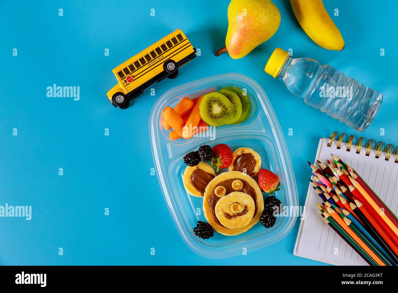 Zurück zur Schule Konzept. Lunchbox mit Pfannkuchen, Karotte, Birne und Banane mit Kinderschrubben. Draufsicht, Kopierbereich. Stockfoto