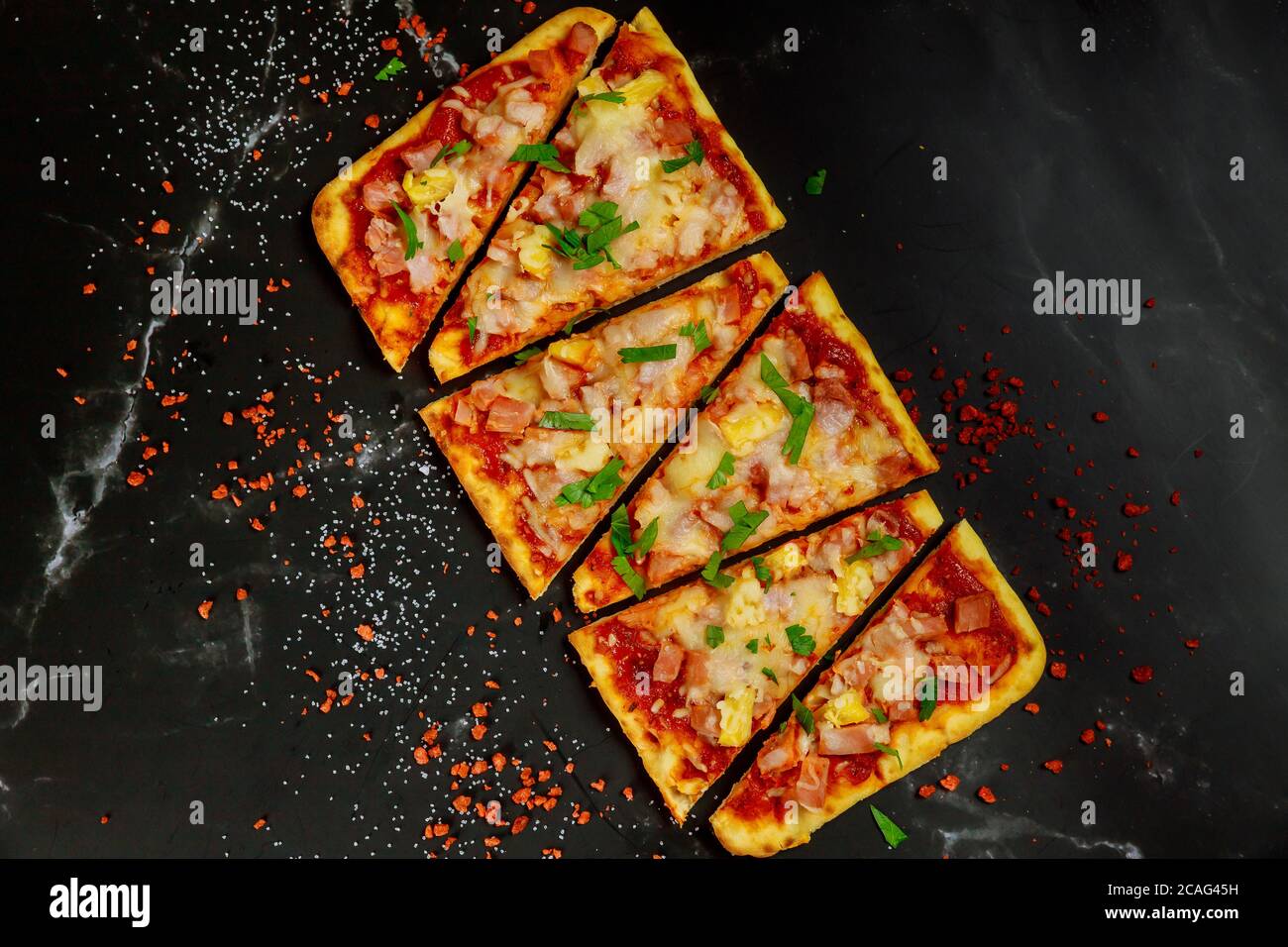 hawaiianische Pizza mit Schinken, Käse und Ananas auf dunklem Grund in Scheiben schneiden. Draufsicht. Stockfoto